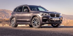 A gray BMW X3 parked on a road with a mountain landscape in the background. The car has a license plate that reads "YK67 AFY."