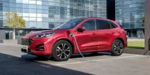 A red Ford Kuga PHEV plugged into a charging point outside an office building.