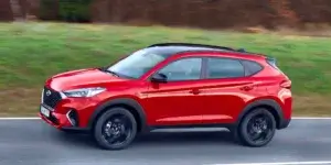 Red Hyundai Tucson driving on a road with trees in the background.