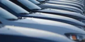 A row of cars parked in a dealership lot. The cars are lined up close together, and only their front hoods are visible.