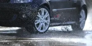 Car with white alloy wheels driving through a puddle, creating water splashes