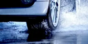 Car with white alloy wheels driving through a puddle, creating water splashes