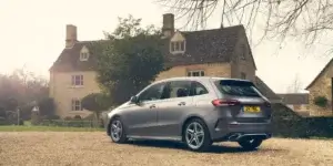 A silver Mercedes-Benz B-Class car parked in a driveway in front of a historic English country house. The car has alloy wheels and a modern design. The license plate on the car is 247 MBC.